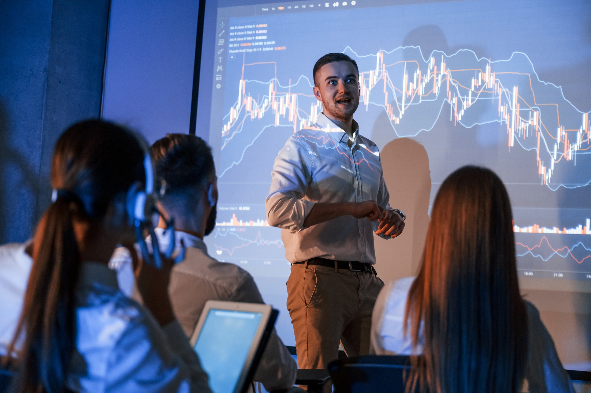 Company growth plan. Male leader talking to employees, showing information on projector in office